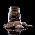 Dark brown smooth river stones arranged in and around a clear glass bottle with a cork stopper, photographed on a glossy black reflective surface against a black background.