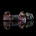Three miniature quilted handbag-shaped objects in brown, blue, and pink, arranged on a glossy black reflective surface against a black background.