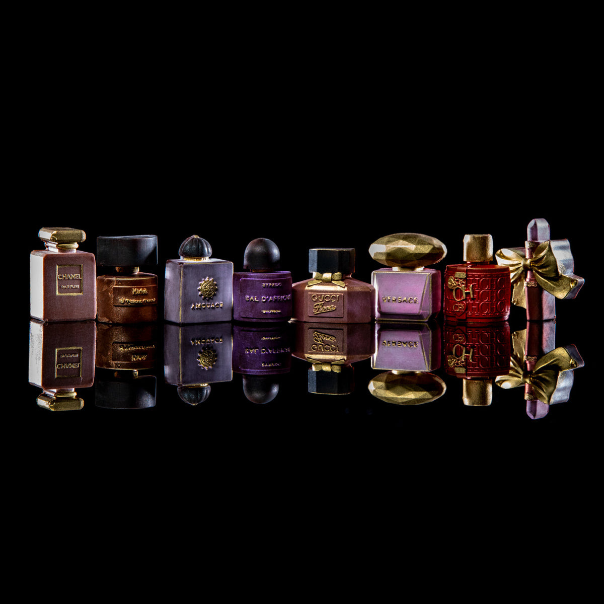A row of vintage-style perfume bottles in purple, red, brown, and gold, arranged on a glossy black reflective surface against a black background.
