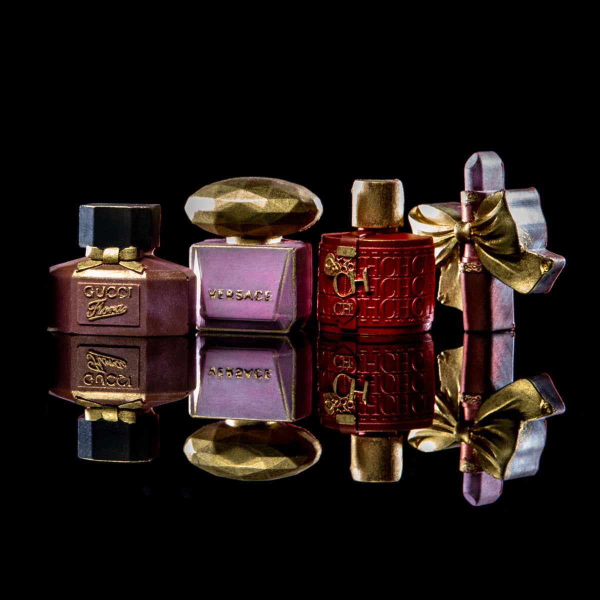 Four luxury perfume bottles arranged on a glossy black reflective surface against a black background. From left to right: a dark mauve Gucci Flower bottle with gold trim and cap, a lavender Versace bottle with a gold dome cap, a deep red CHANEL perfume bottle with gold detailing, and a lavender Versace bottle tied with a gold ribbon.