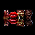 Four novelty chocolate sculptures arranged on a glossy black reflective surface: a red mini dress, red lips, a brown gift box with gold bow, and a brown muscular torso. No person, animal, or real environment is present, so this is Product/Packaging.