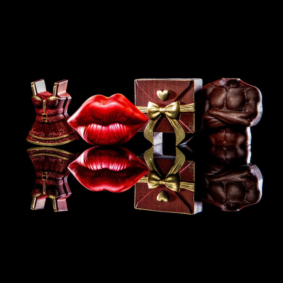 Four novelty chocolate sculptures arranged on a glossy black reflective surface: a red mini dress, red lips, a brown gift box with gold bow, and a brown muscular torso. No person, animal, or real environment is present, so this is Product/Packaging.